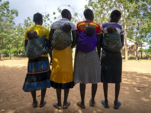 women lined up carrying children on back